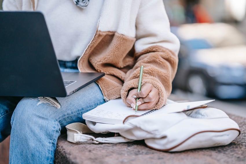 Student writing in a planner while looking at laptop