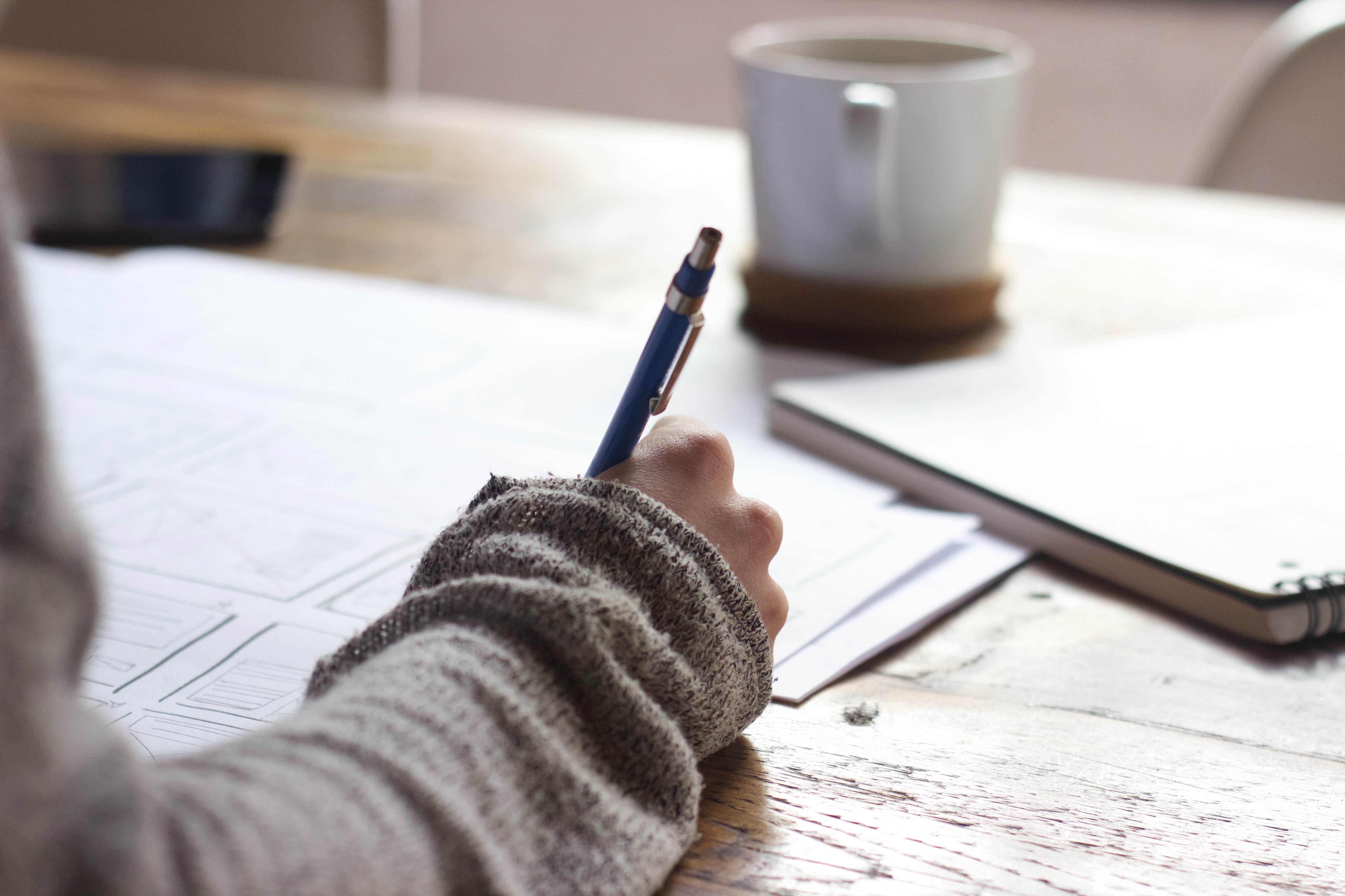 person writes in a notebook on a desk