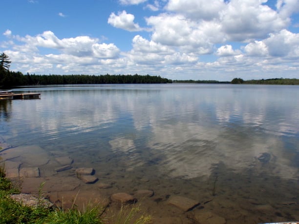 A scene of Duck Lake. The water is calm and clear, and the blue sky is full of fluffy clouds. 