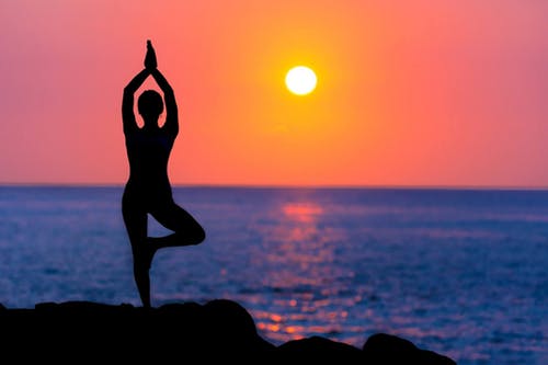 Person doing yoga by the water at sunset.