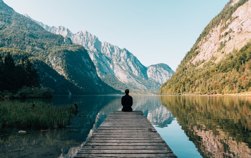 Person sitting on the end of a dock in front of a mountain scape