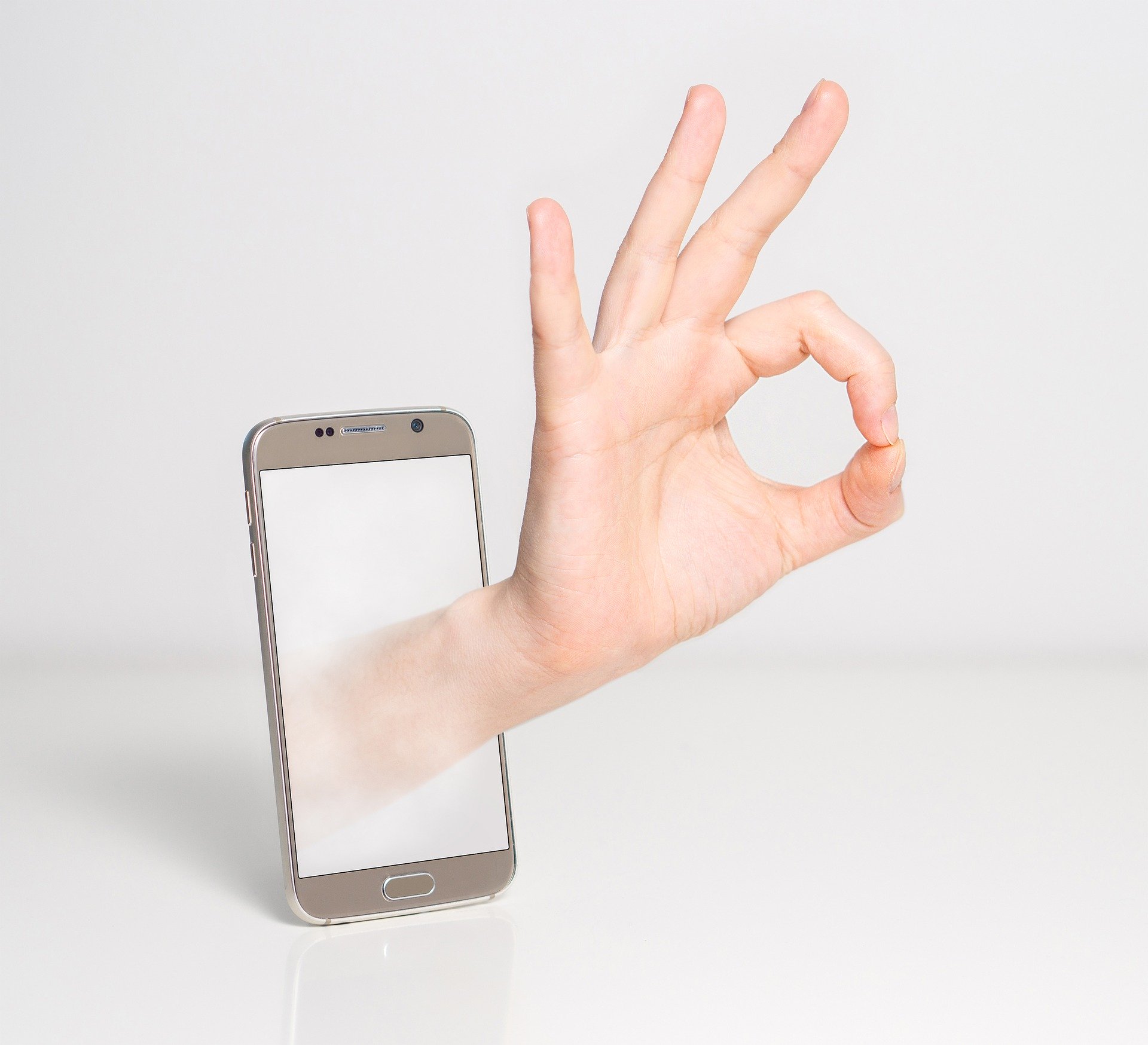 Fingers making the OK symbol coming out of a cellphone