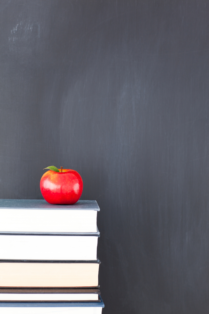 Stack of books with red apple and clean blackboard